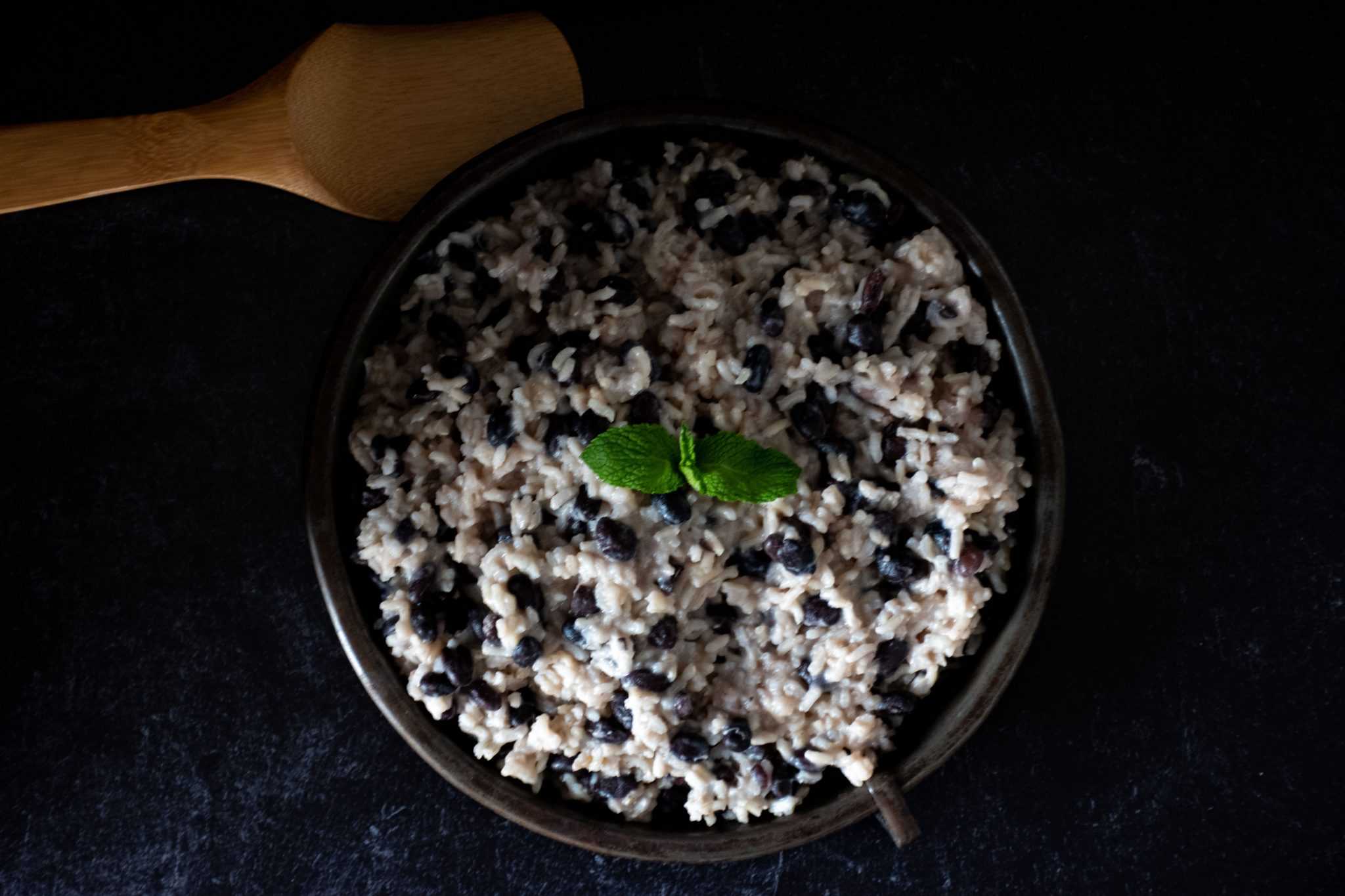 Banana coconut rice and black beans on a round metal plate, garnished with mint, on a dark background with dramatic shadows.
