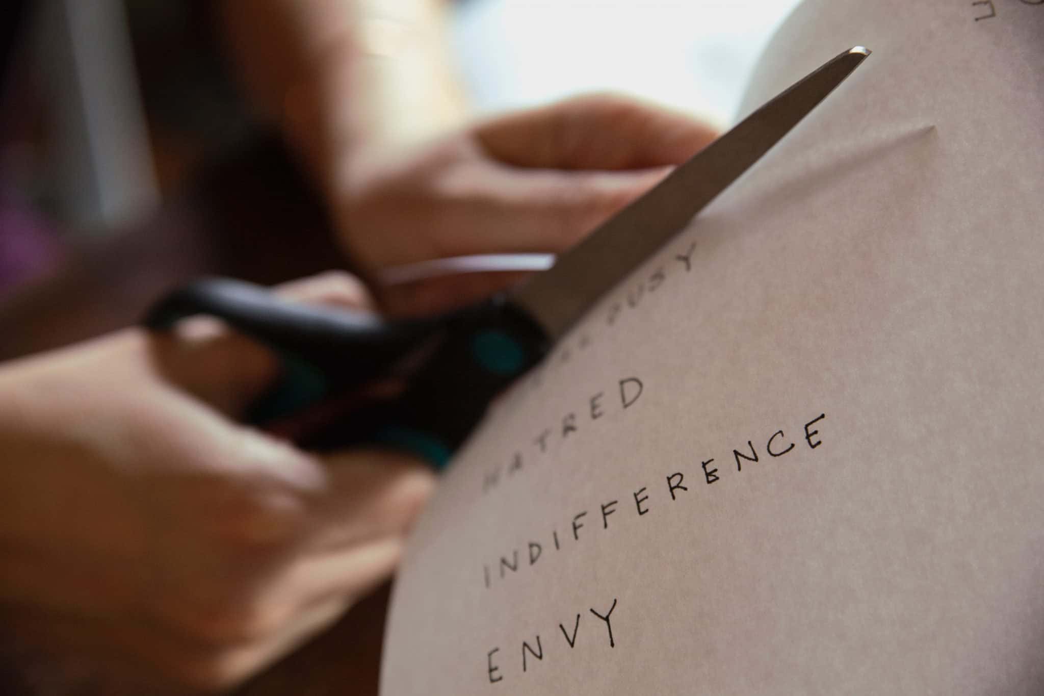 What to give up for Lent: Someone cutting up a paper that reads "Hatred" "Indifference" and "Envy"