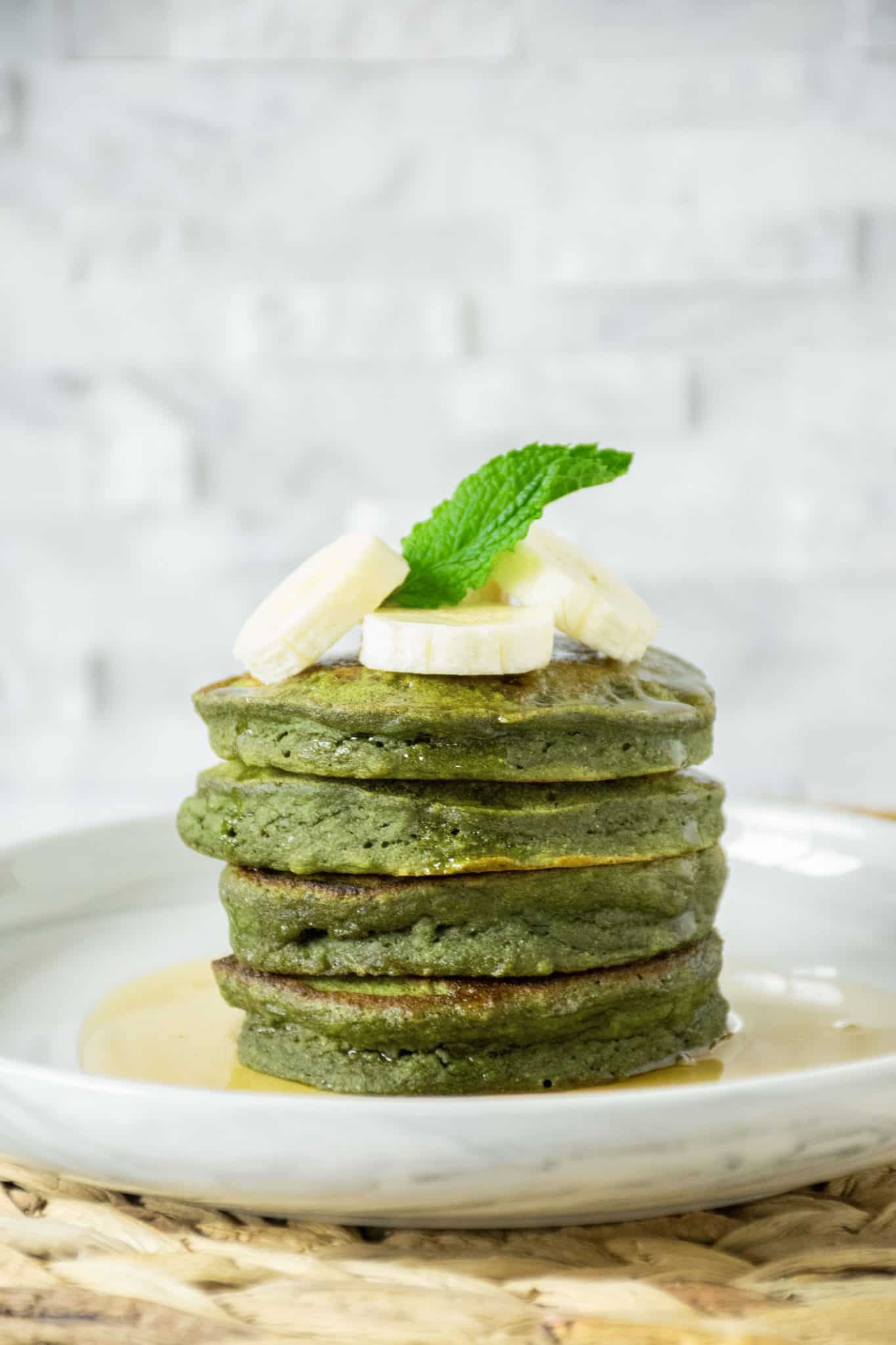 Stack of 4 Banana Mint Pancakes with banana slices and a mint leaf on top.