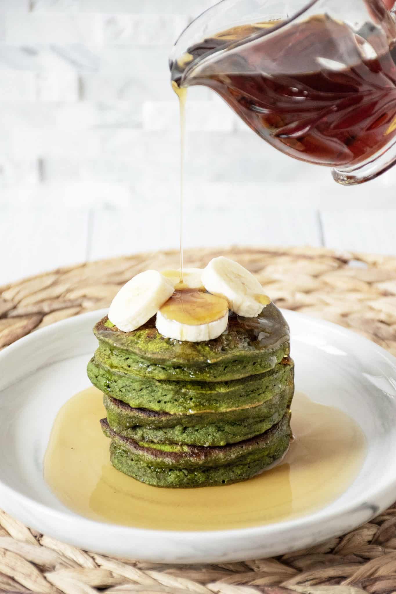 Banana Mint Pancakes on a plate, with banana slices on top, being drizzled with syrup