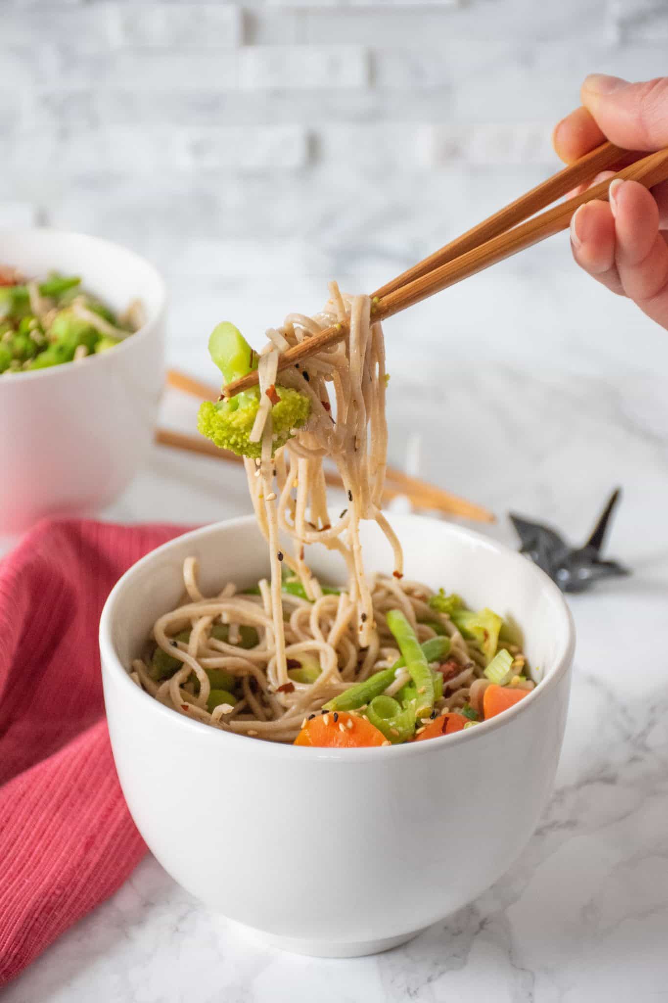 Teriyaki Soba Noodles in a large white bowl, being lifted with chop sticks