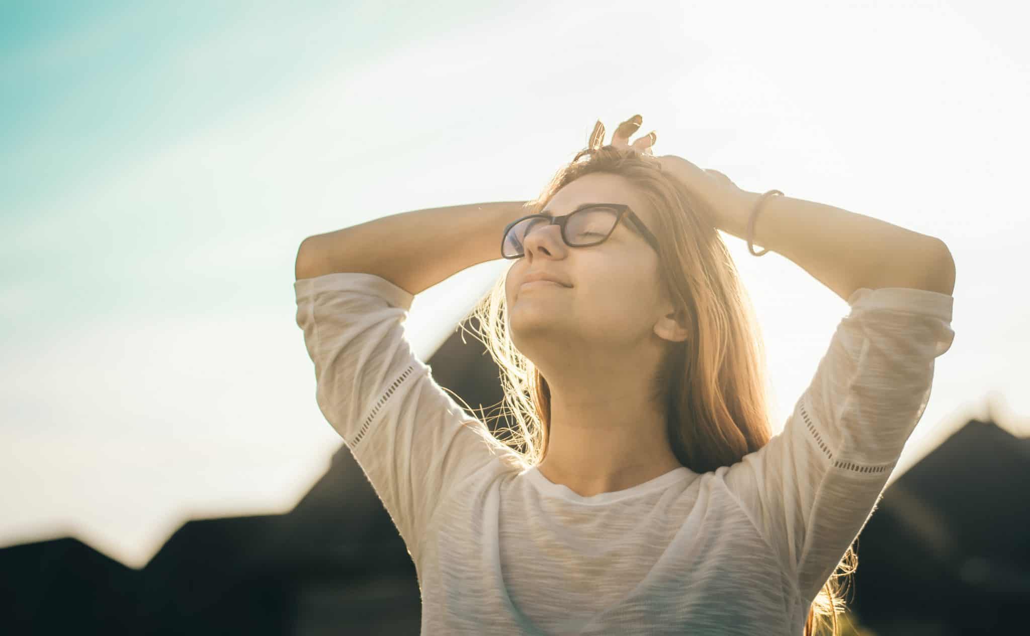 Woman outside, with hands on head, and face turned toward the sky, breathing deeply.