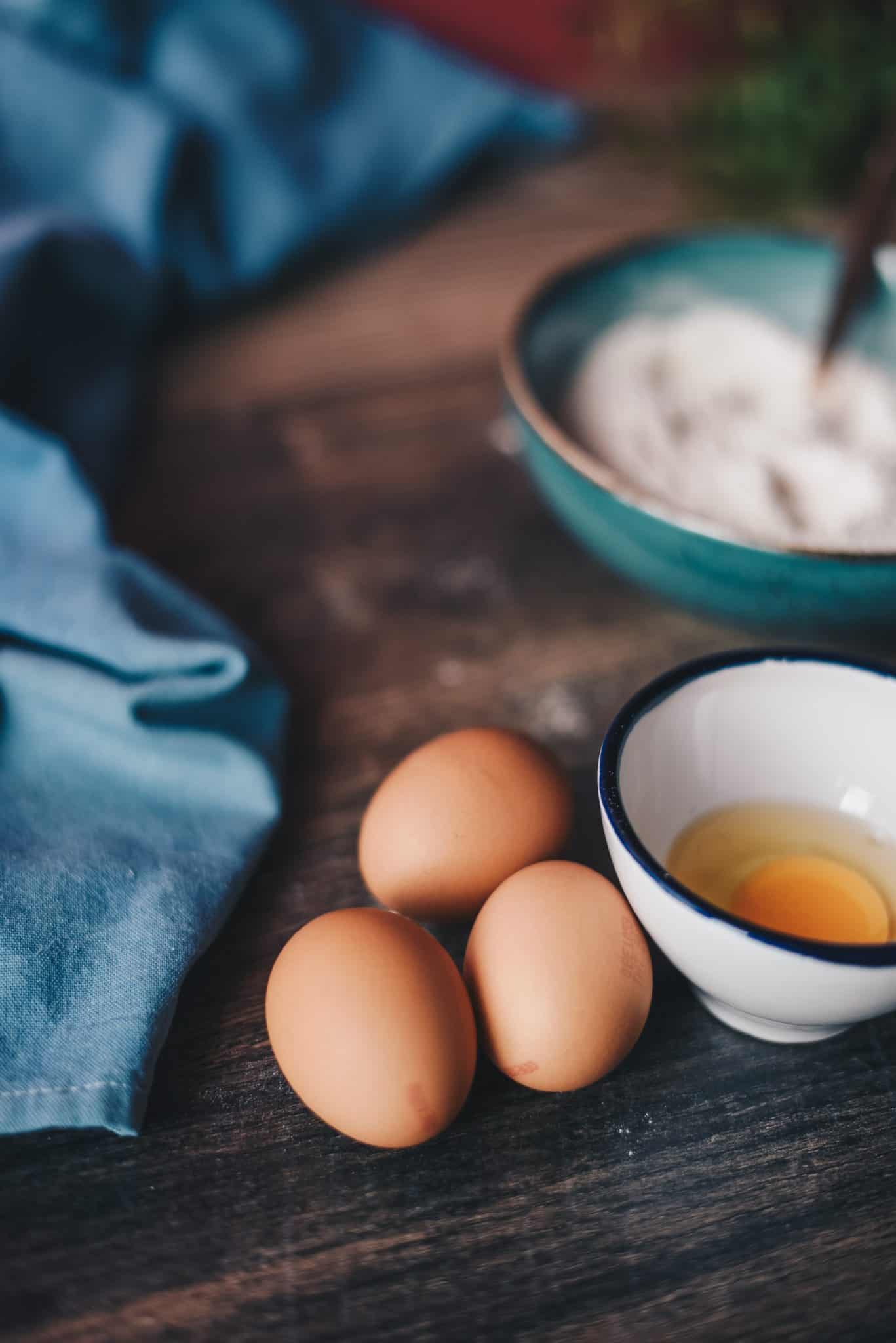 Brown eggs on a table beside a white bowl.