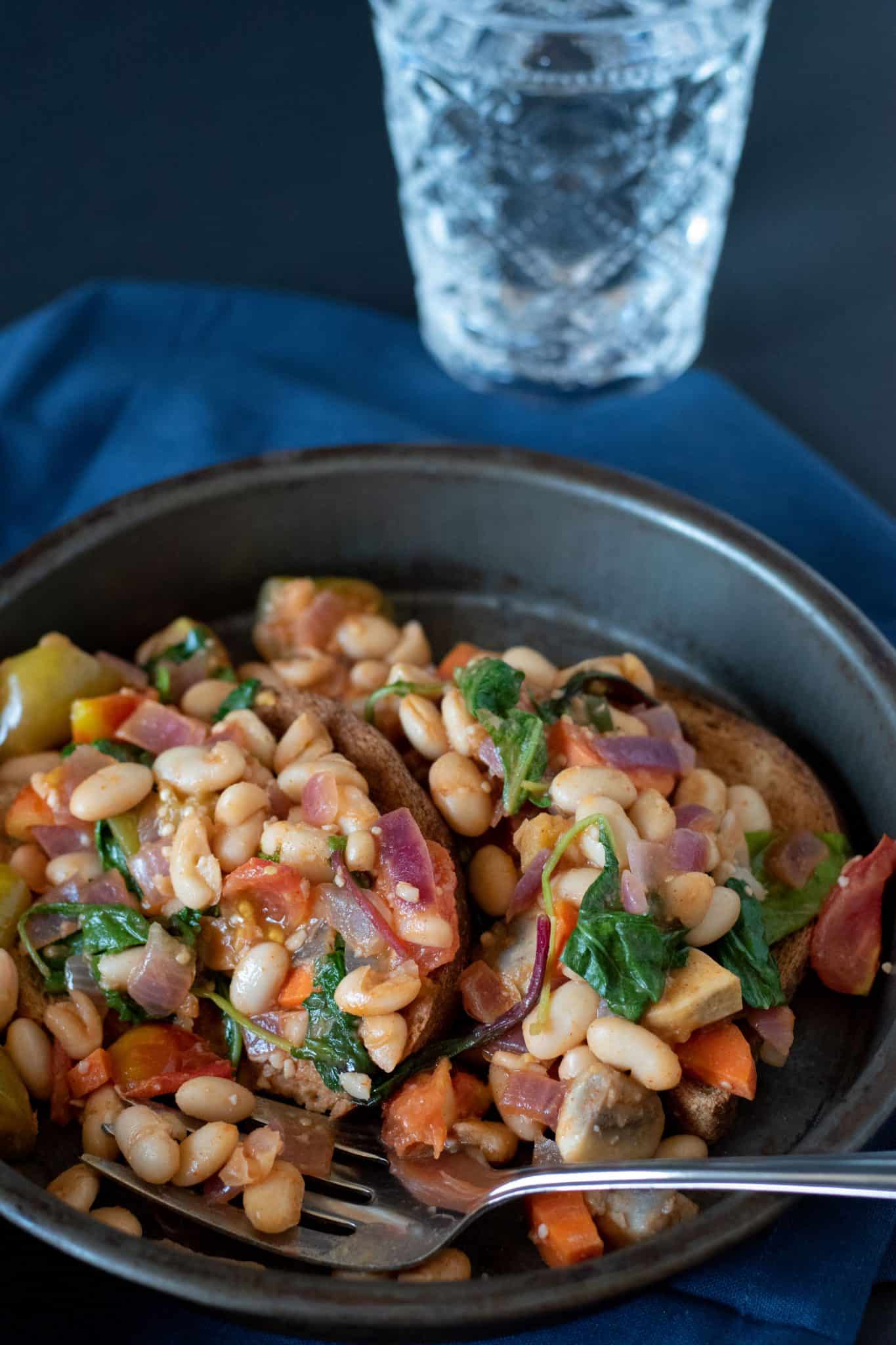 Beans and Greens Breakfast Hash on toast in a metal dish with a fork.