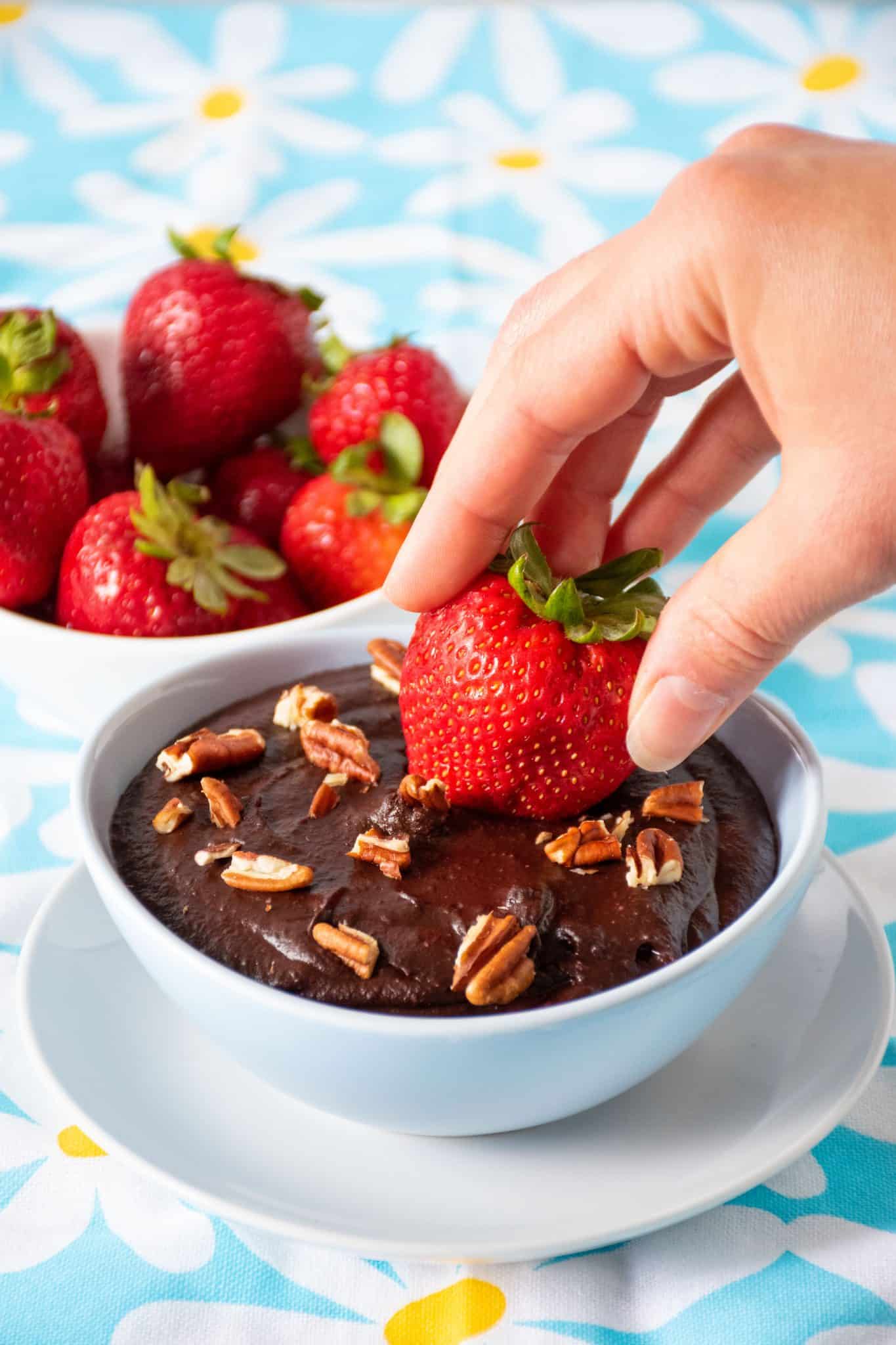 a strawberry being dipped into a bowl of brownie batter dip.