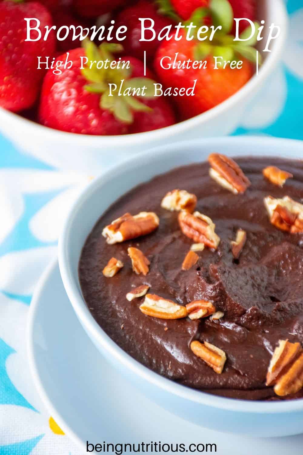 Brownie batter dip in a bowl with pecan pieces on top, and a bowl of strawberries behind.