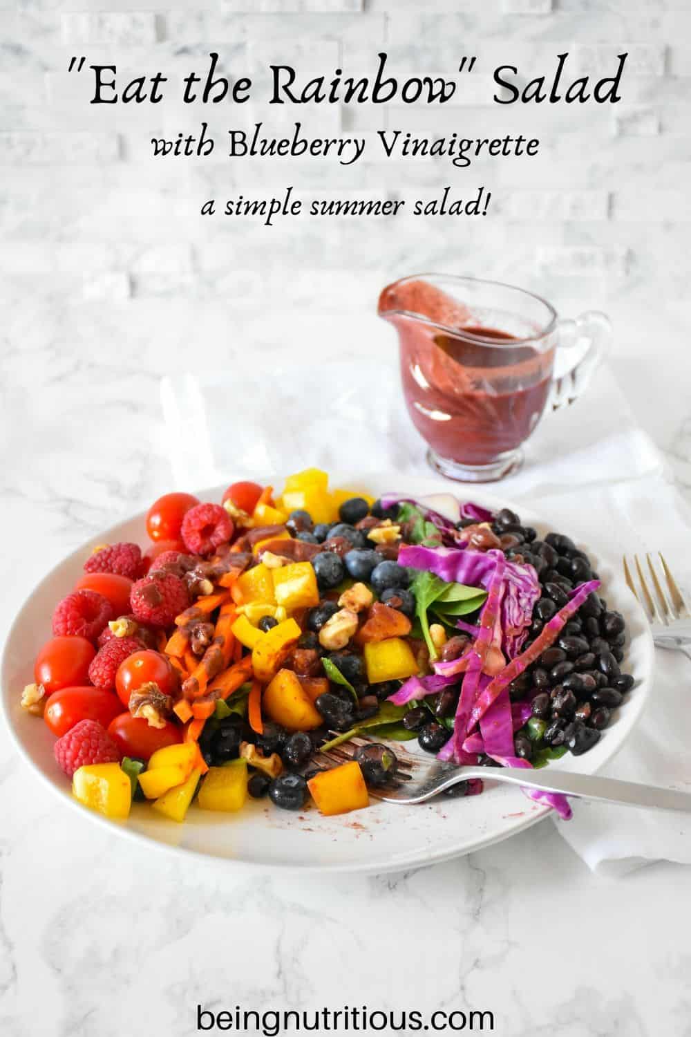Rainbow salad on a plate, with blueberry vinaigrette dressing poured on, and several bites take from salad.