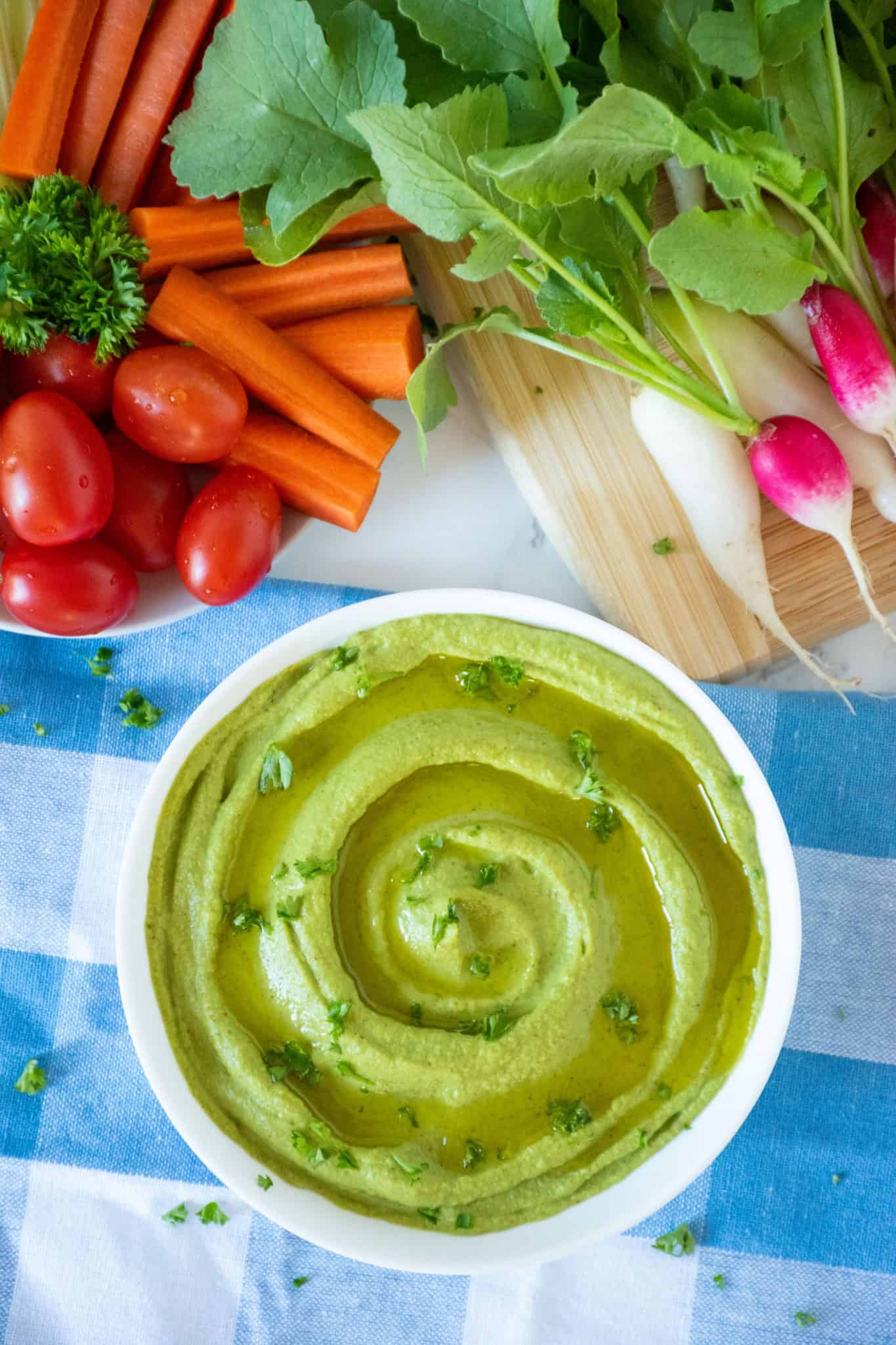 Overhead shot of radish greens hummus in a bowl with a variety of vegetables surrounding the bowl.