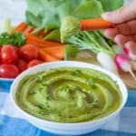 Radish Greens Hummus in a bowl with a hand dipping a carrot stick in it.