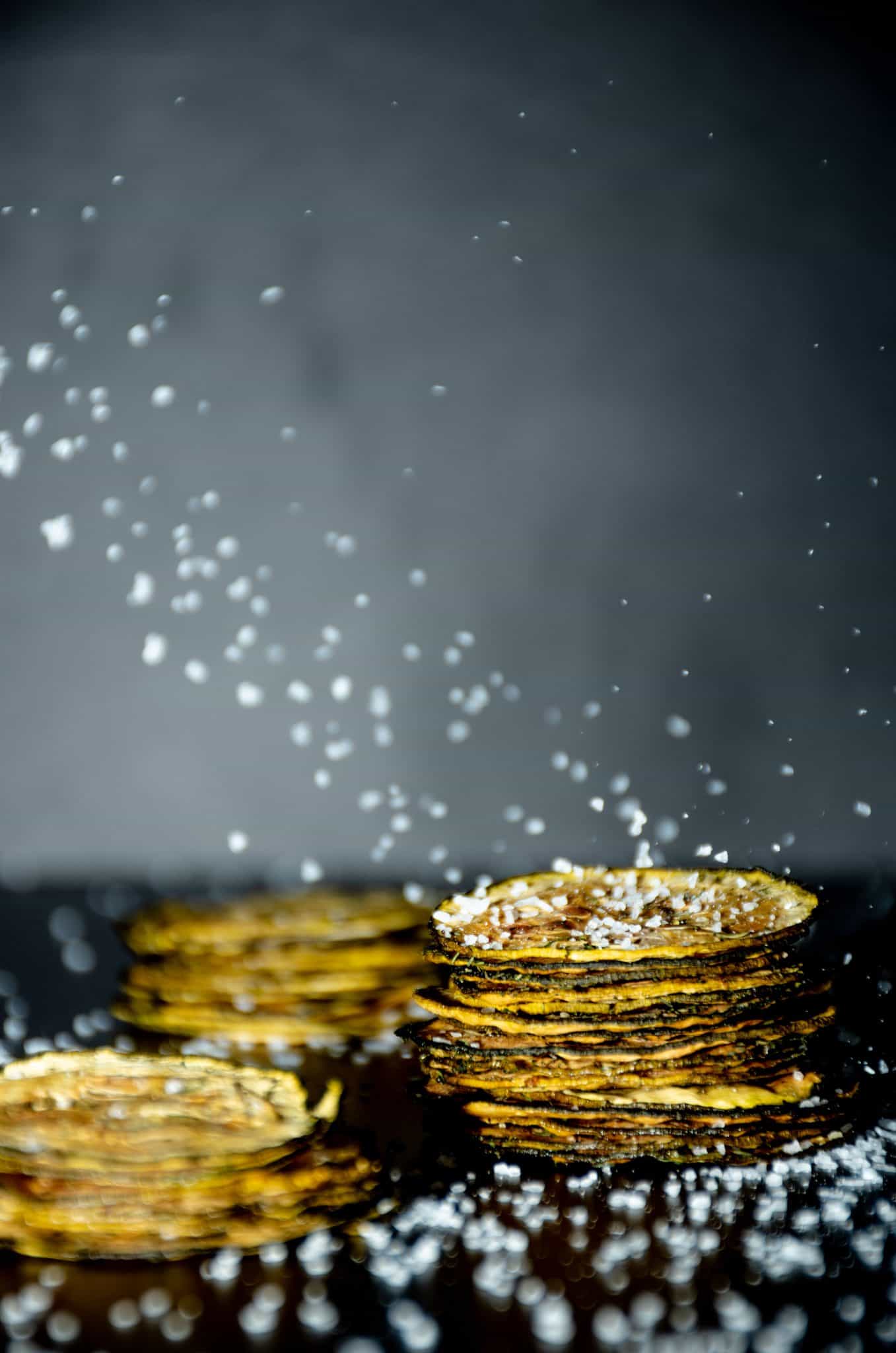 Image of 3 stacks of zucchini chips, with salt crystals falling all around.