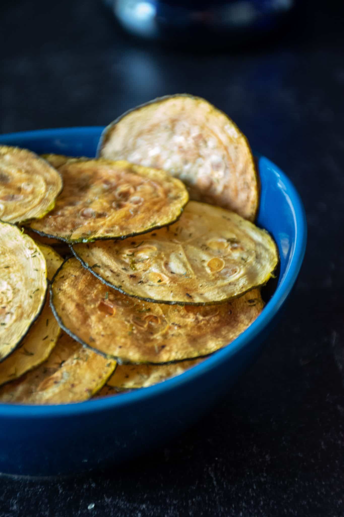 Zucchini chips in a blue bowl in front of dark background.