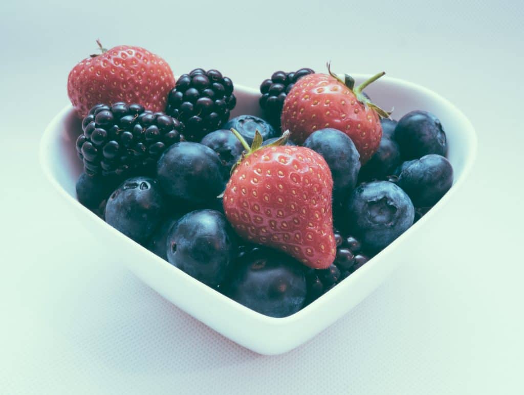 blueberries, blackberries, and strawberries in white, heart-shaped bowl