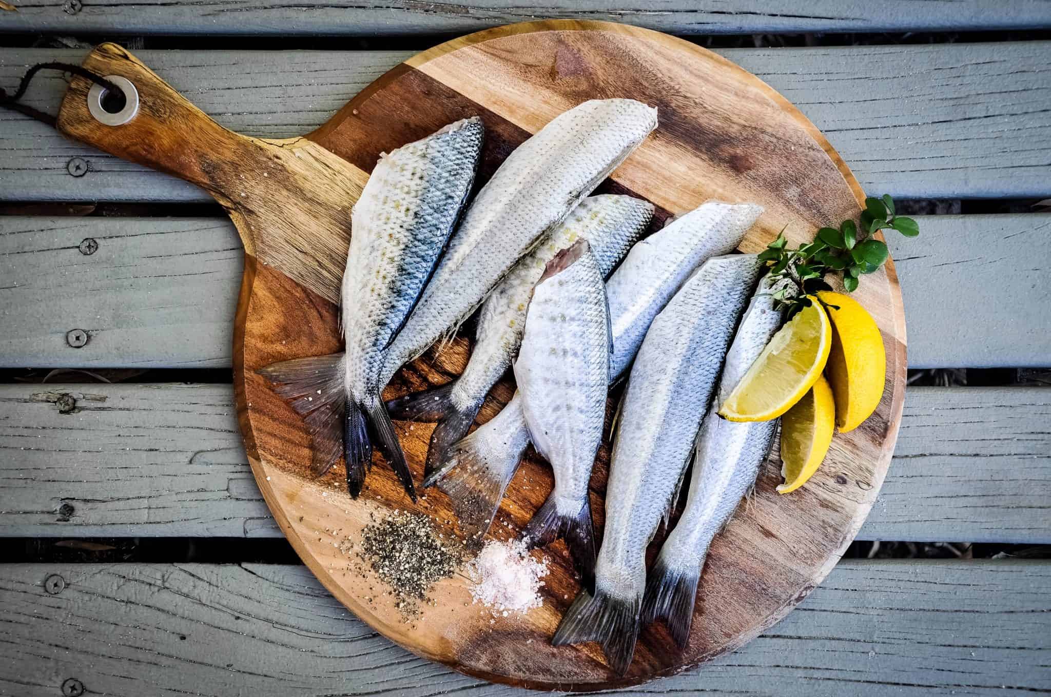 Seven butchered fish on a round cutting board, with lemon slices and salt and pepper