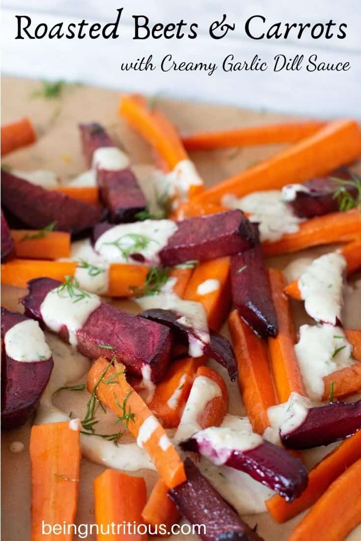 Close up of beets and carrots, cut into thick sticks, roasted, drizzled with garlic dill sauce, on the baking sheet. Text overlay: Roasted Beets and Carrots with creamy garlic dill sauce.