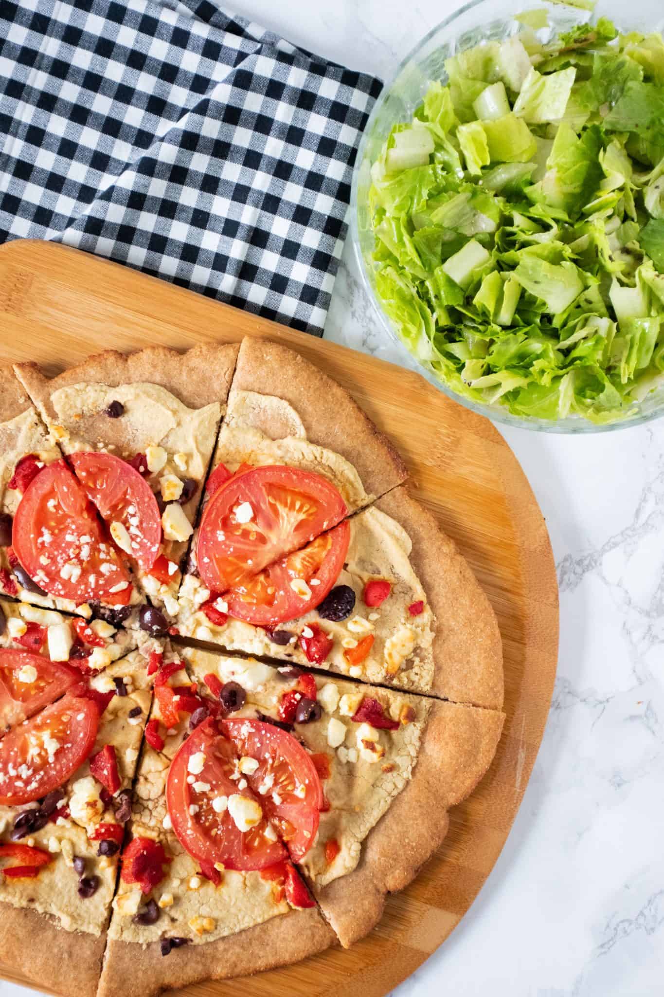 Whole grain pizza on a peel, with bowl of salad in background.