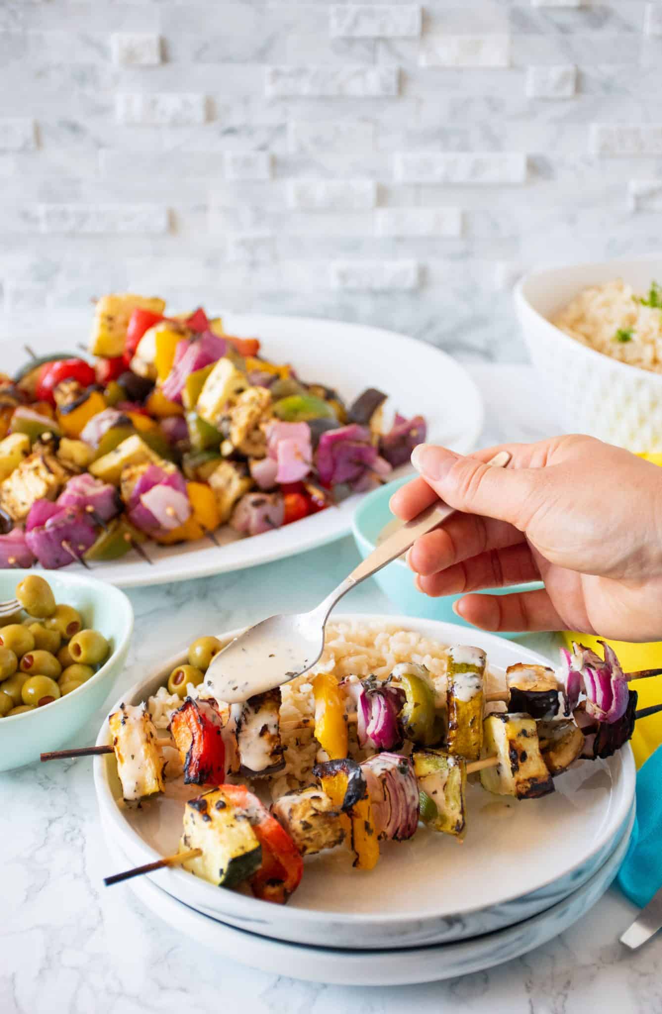 Plate with 2 veggie skewers and rice, with marinade being drizzled over.