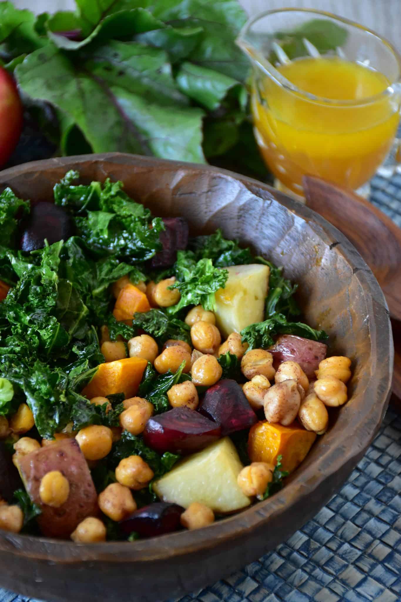 Kale salad in a wooden bowl with apple maple vinaigrette in the background.