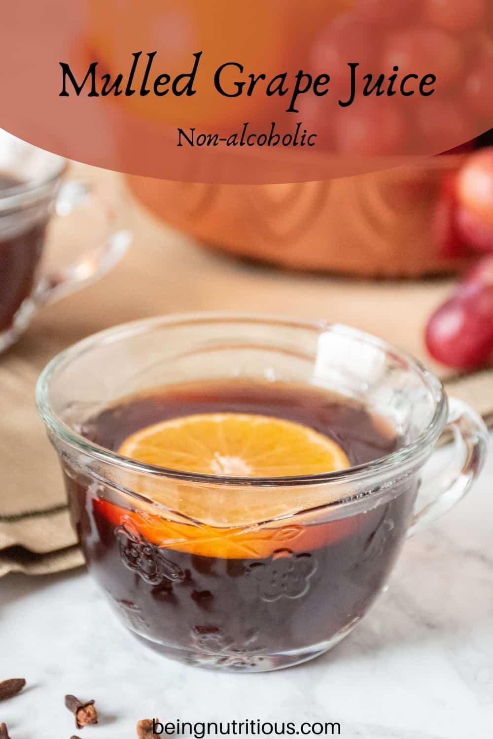 Close up of a small glass mug, filled with mulled grape juice, with an orange slice in it. Text overlay: mulled grape juice; non-alcoholic.