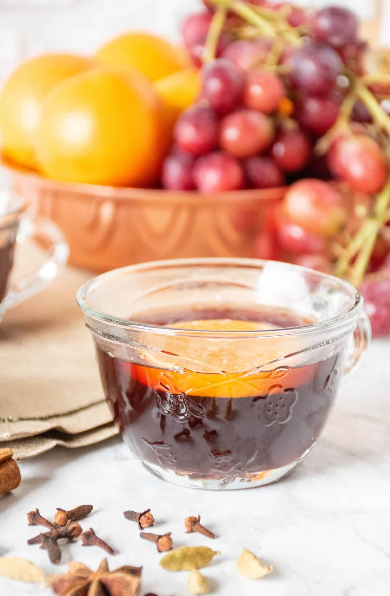 Close up of a small glass mug, filled with mulled grape juice, with an orange slice in it.