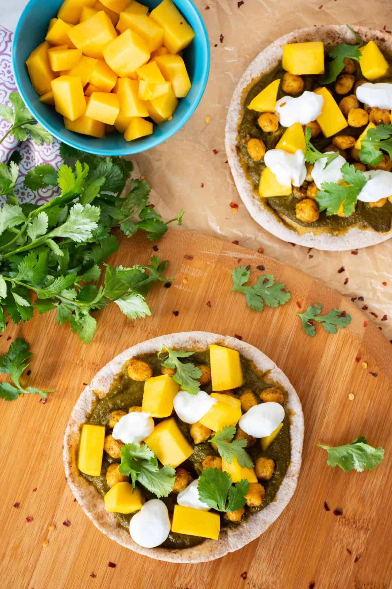 Overhead shot of pizza with spinach sauce, chickpeas, and mangoes on mini pitas.