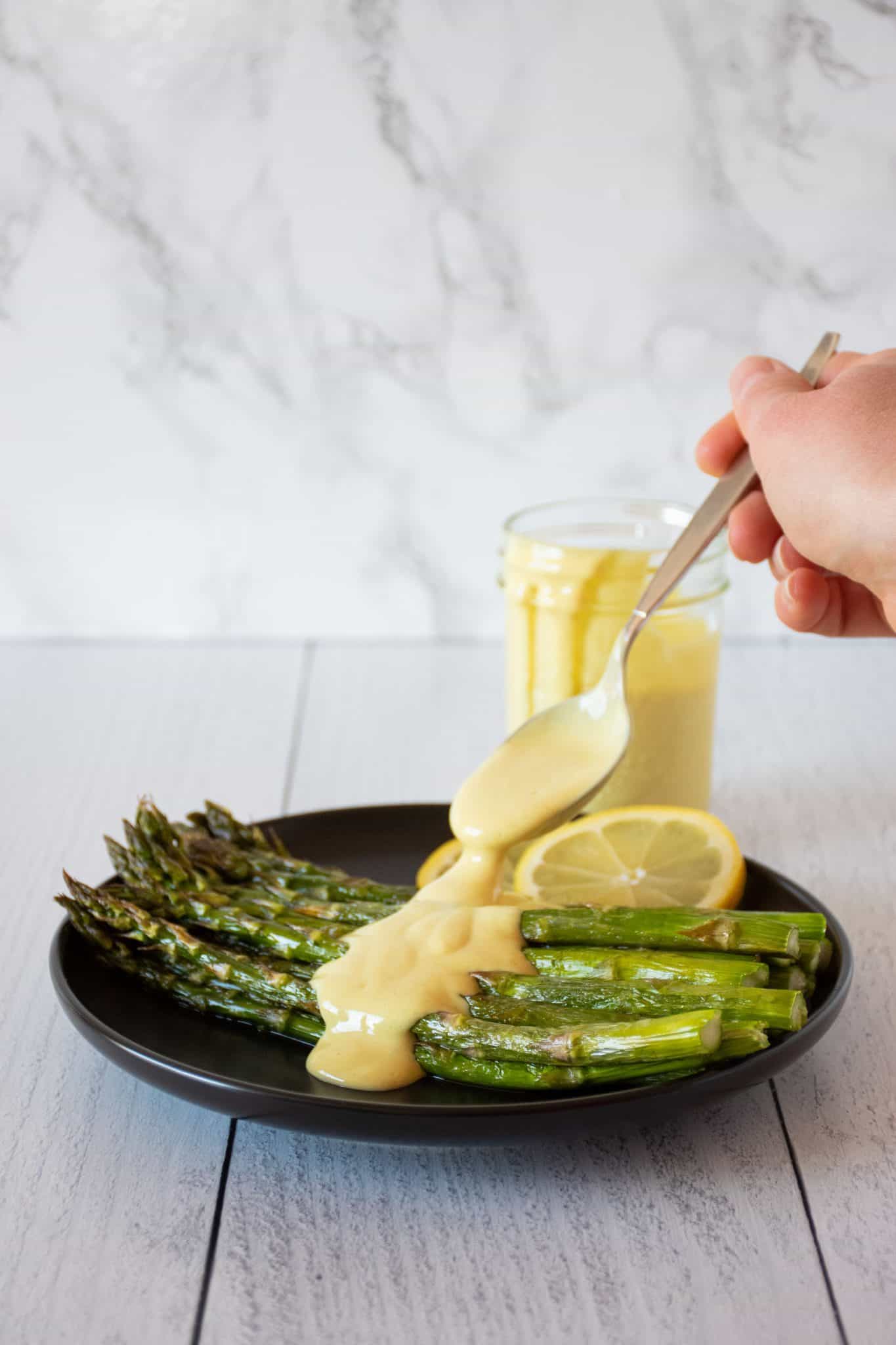 Plate of asparagus being drizzled with sauce.