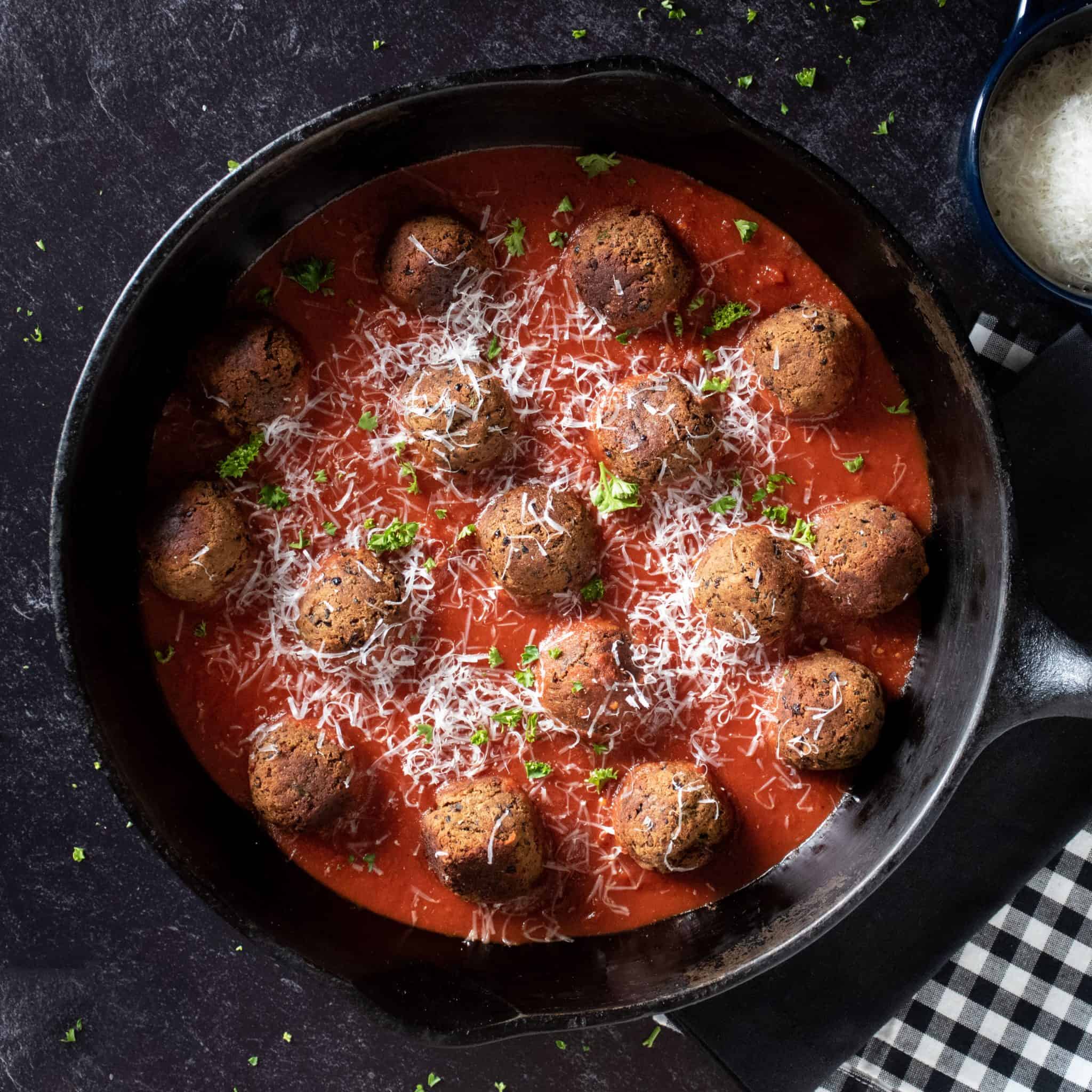 meatballs made of black beans in a large cast iron skillet with marinara sauce.