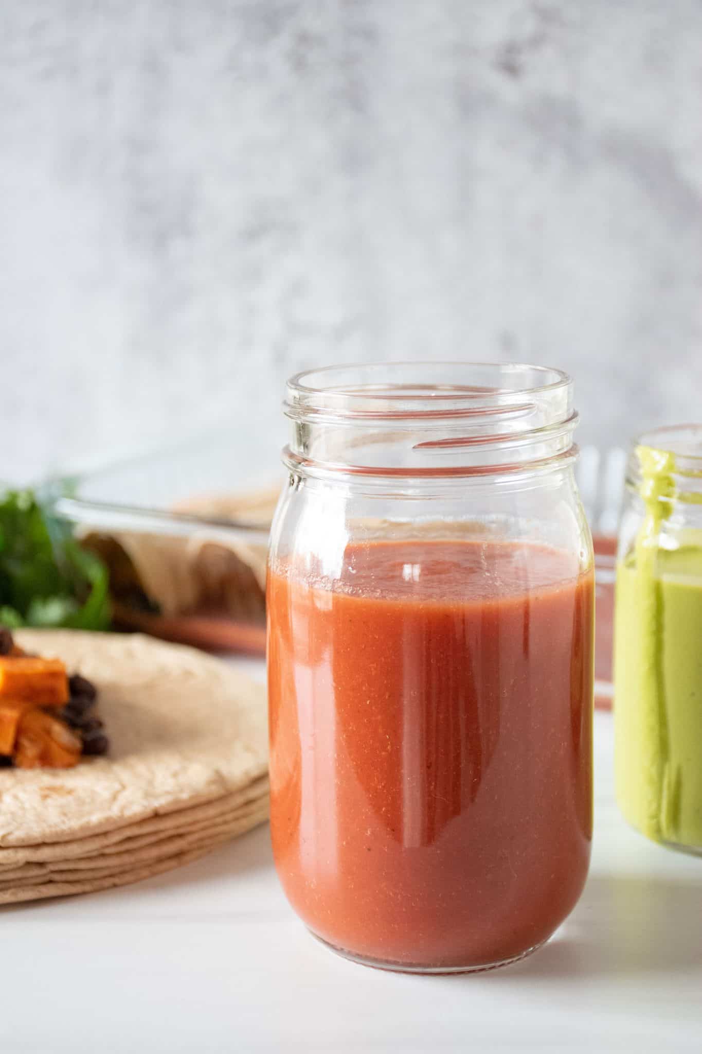 Red sauce in a jar, with enchiladas being made in the background.