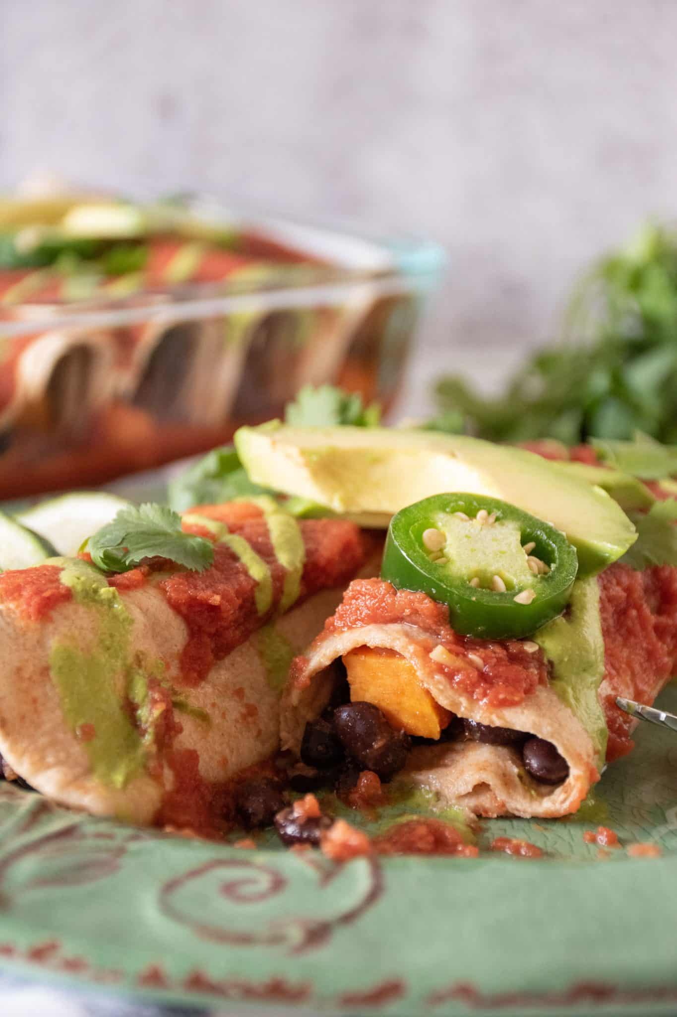 Close up of enchiladas on a plate with cilantro, lime, jalapeno slices, and avocado.