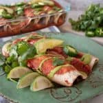 Two enchiladas on a plate, with cilantro, lime slices, jalapeno slices, and avocado.