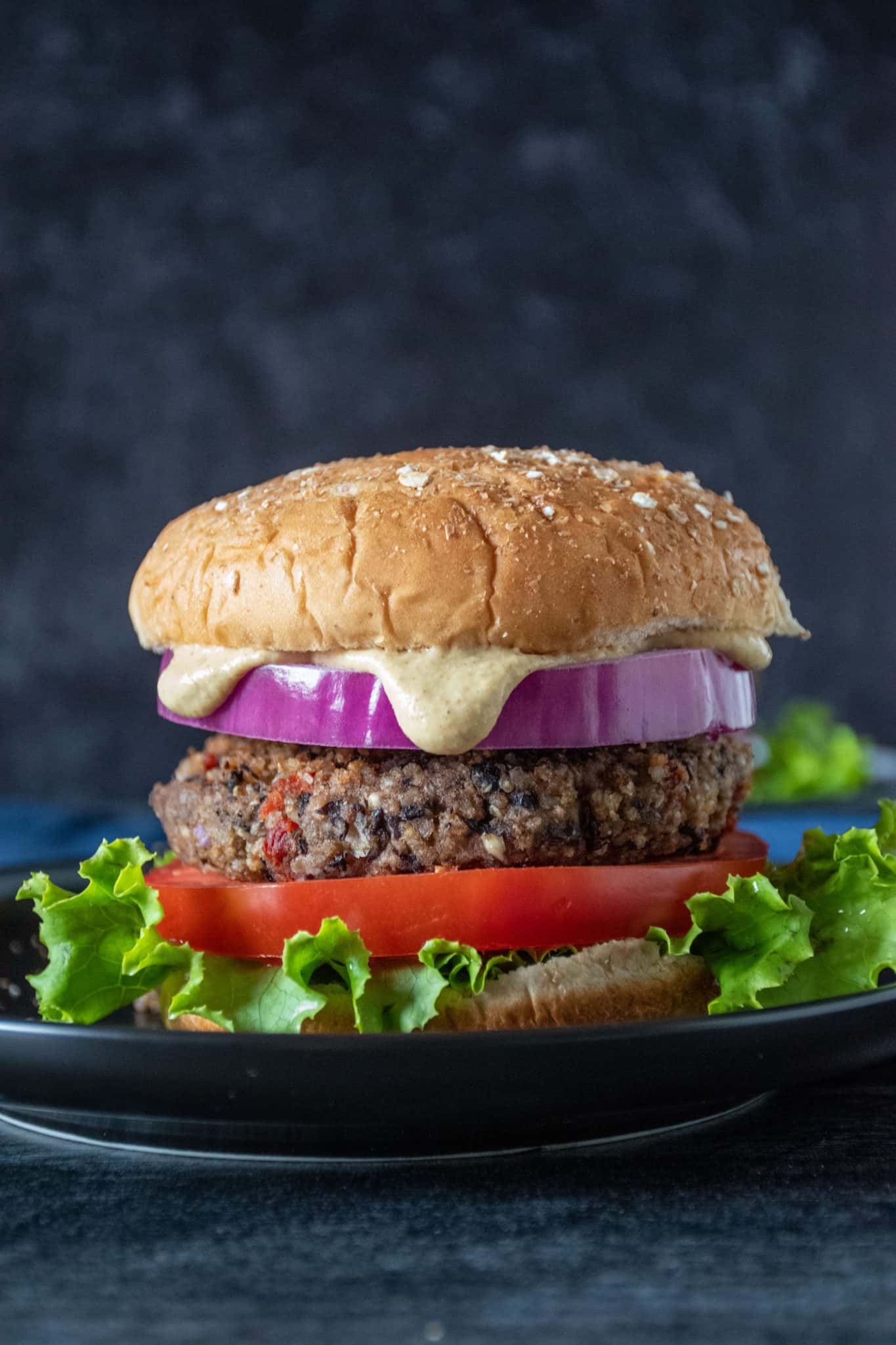 Bean burger on a bun, with onions, tomatoes, lettuce and sauce dripping out.