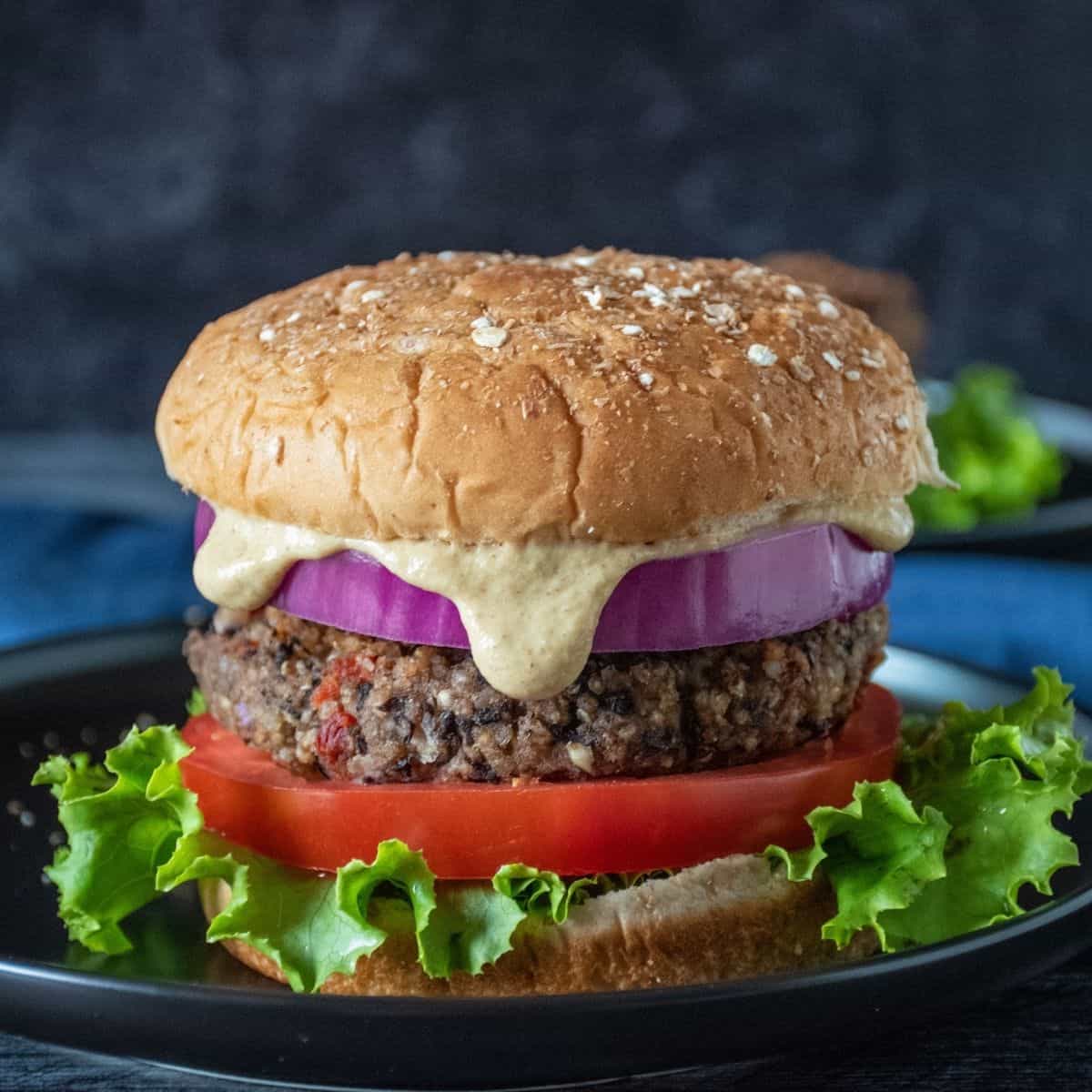 Bean burger on a bun, with onions, tomatoes, lettuce and sauce dripping out.