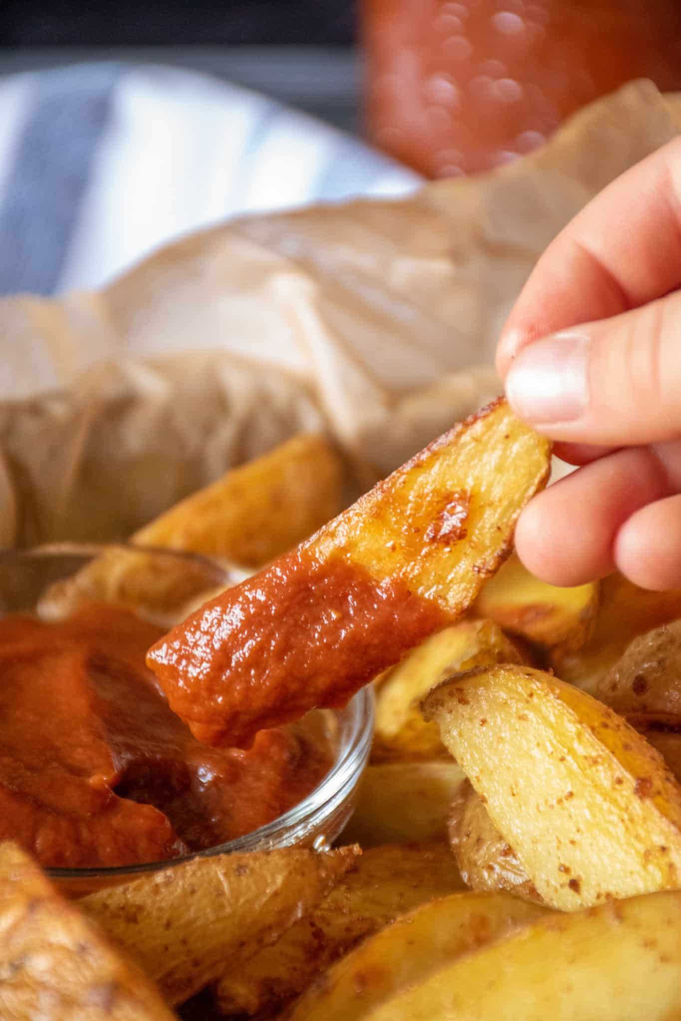 Hand holding a potato wedge, dipped in ketchup.