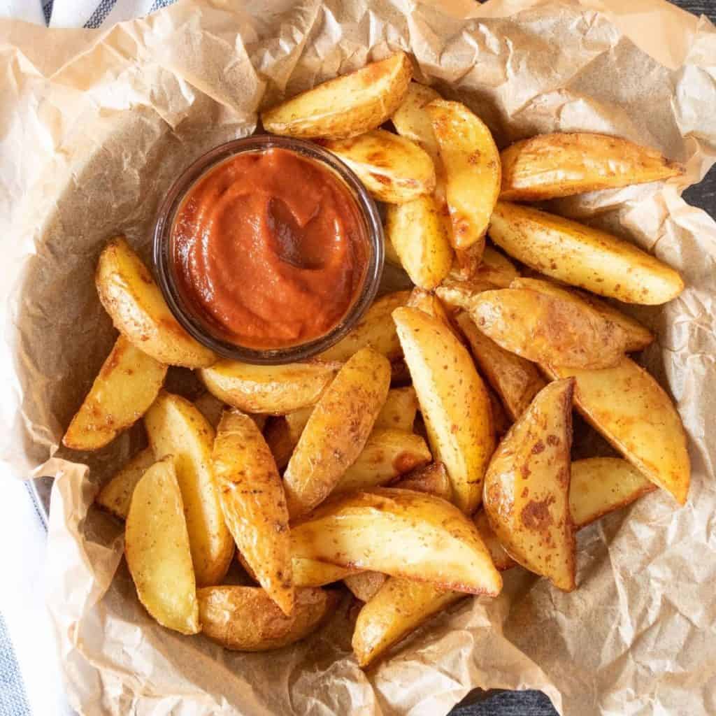 Basket of potato wedges with a small bowl of ketchup.