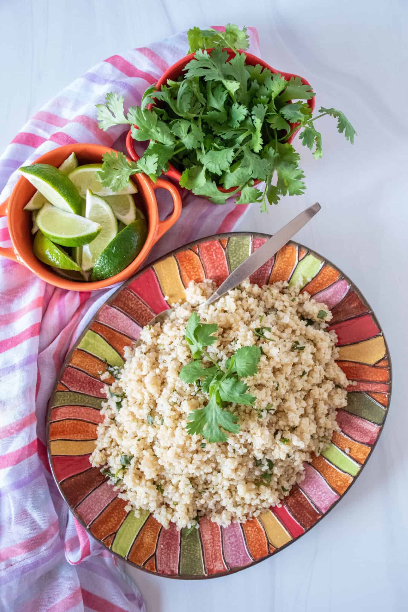 Overhead picture of quinoa on a plate, with small bowls of limes slices and fresh cilantro above.