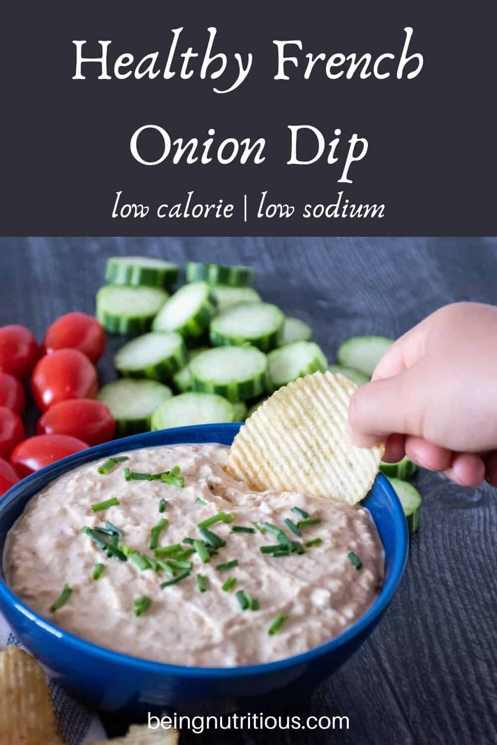 Bowl of dip, surrounded by chips, cucumber slices, and baby tomatoes. Hand holding a chip with dipping it. Text overlay: Healthy French Onion Dip, low calorie, low sodium.