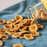 Dehydrated banana chips spilling out of a glass jar.