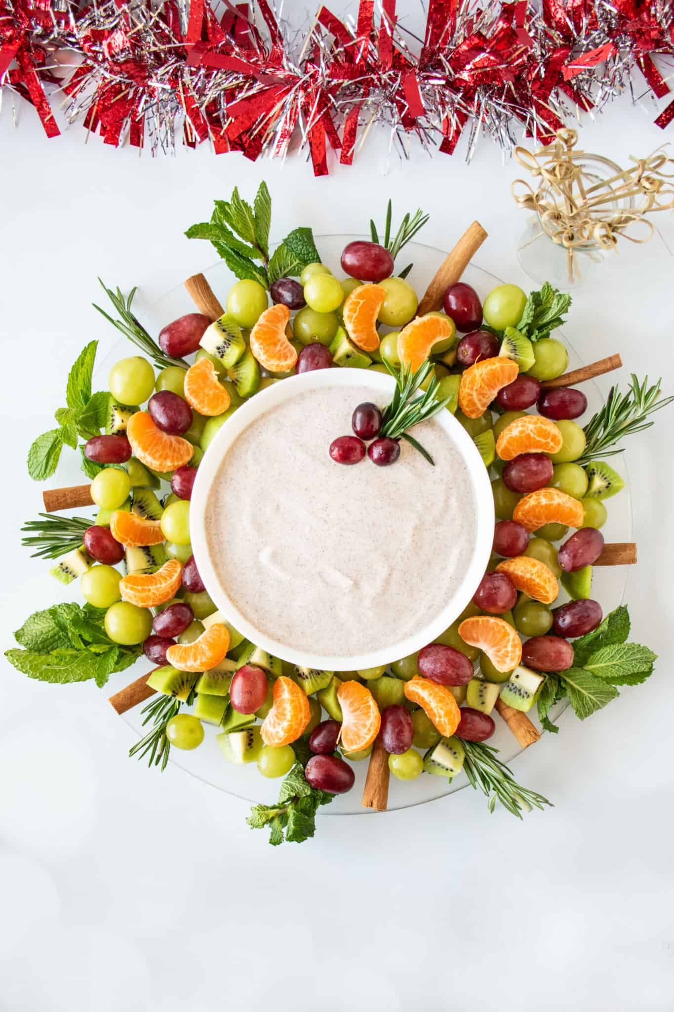 A winter fruit salad shaped like a wreath, with a bowl of dip in the middle.