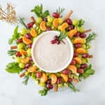 A winter fruit salad shaped like a wreath, with a bowl of dip in the middle.