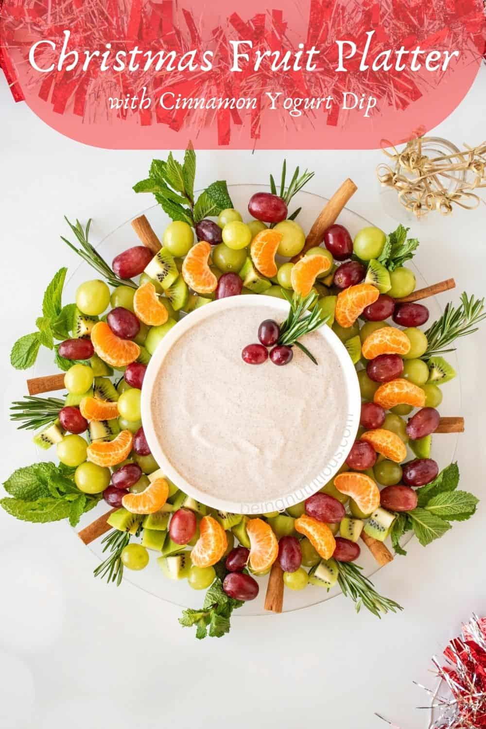A winter fruit salad shaped like a wreath, with a bowl of dip in the middle. Text overlay: Christmas Fruit Platter, with Cinnamon Yogurt Dip. data-pin-description=