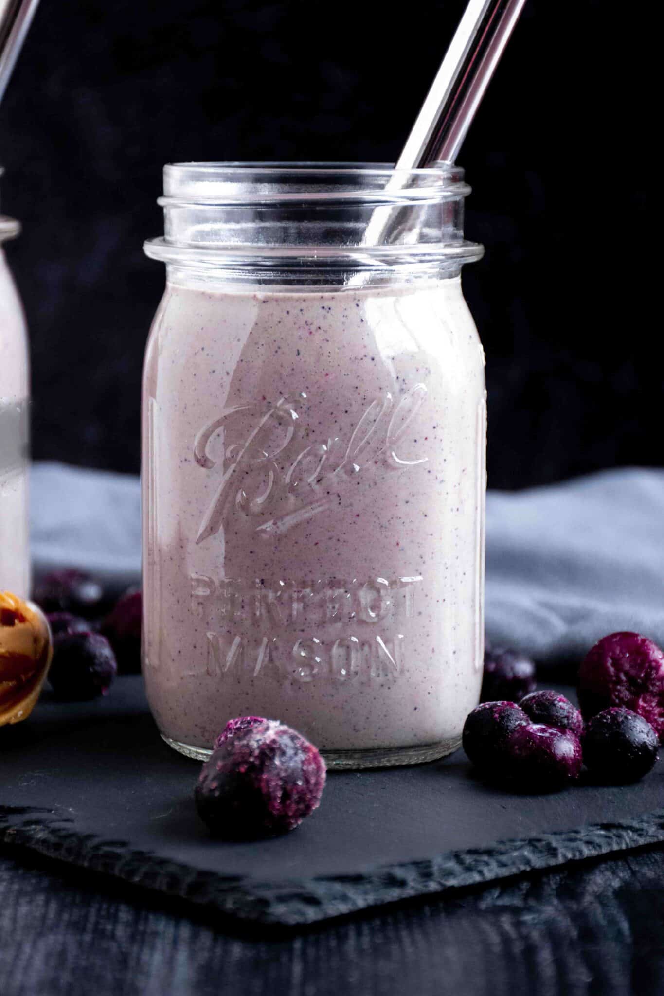 Berry smoothie in a mason jar, with frozen berries scattered around the outside.