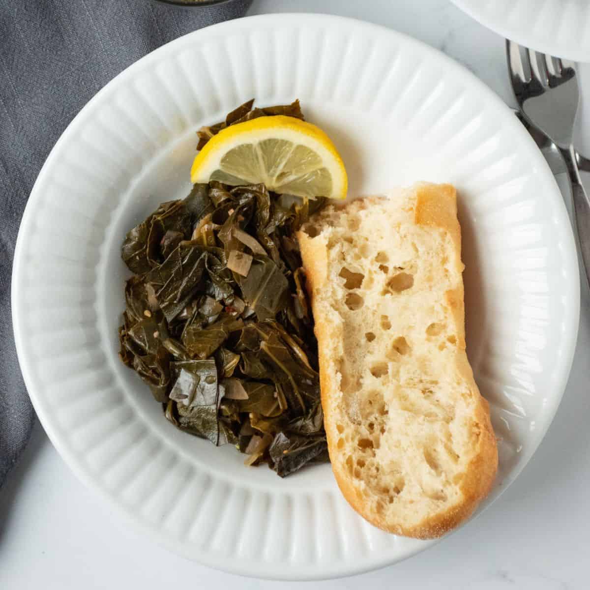 Bowl with collard greens and crusty bread, garnished with a lemon slice.