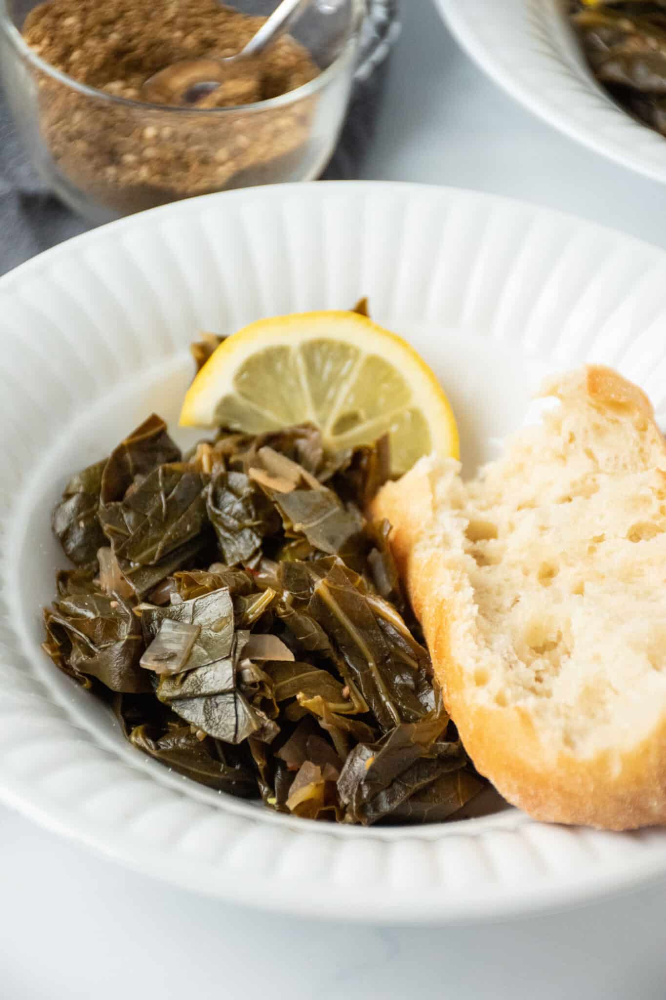 Bowl with collard greens and crusty bread, garnished with a lemon slice.