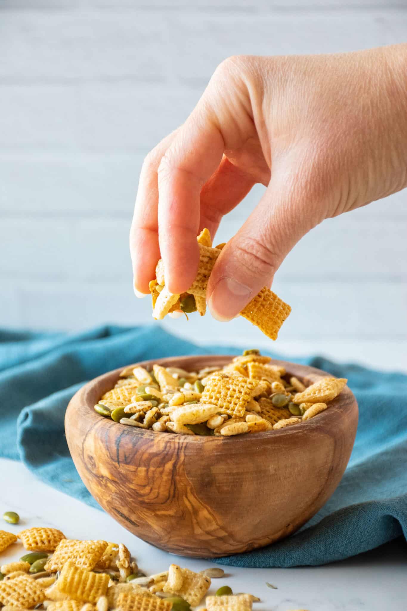 Hand reaching into a bowl of Chex mix.