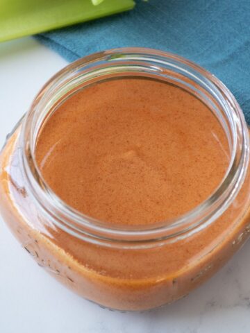Buffalo sauce in a small jar, with celery sticks in the background.