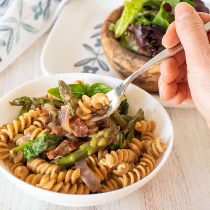 A fork with creamy vegetable pasta being lifted out of a bowl of the pasta.