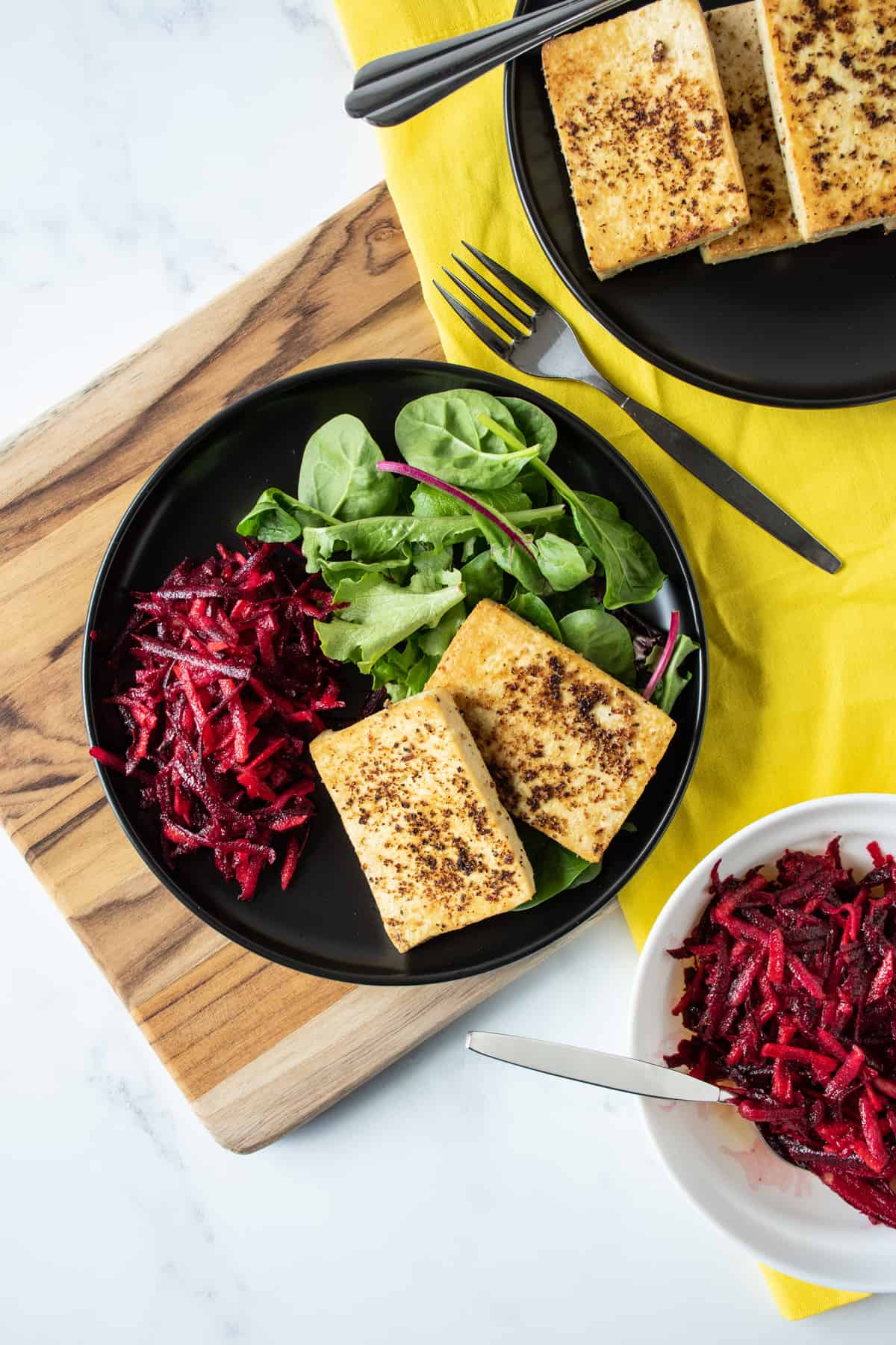Overhead image of a plate with 2 slices of cooked tofu over a bed of greens, and a side of shredded beet salad.
