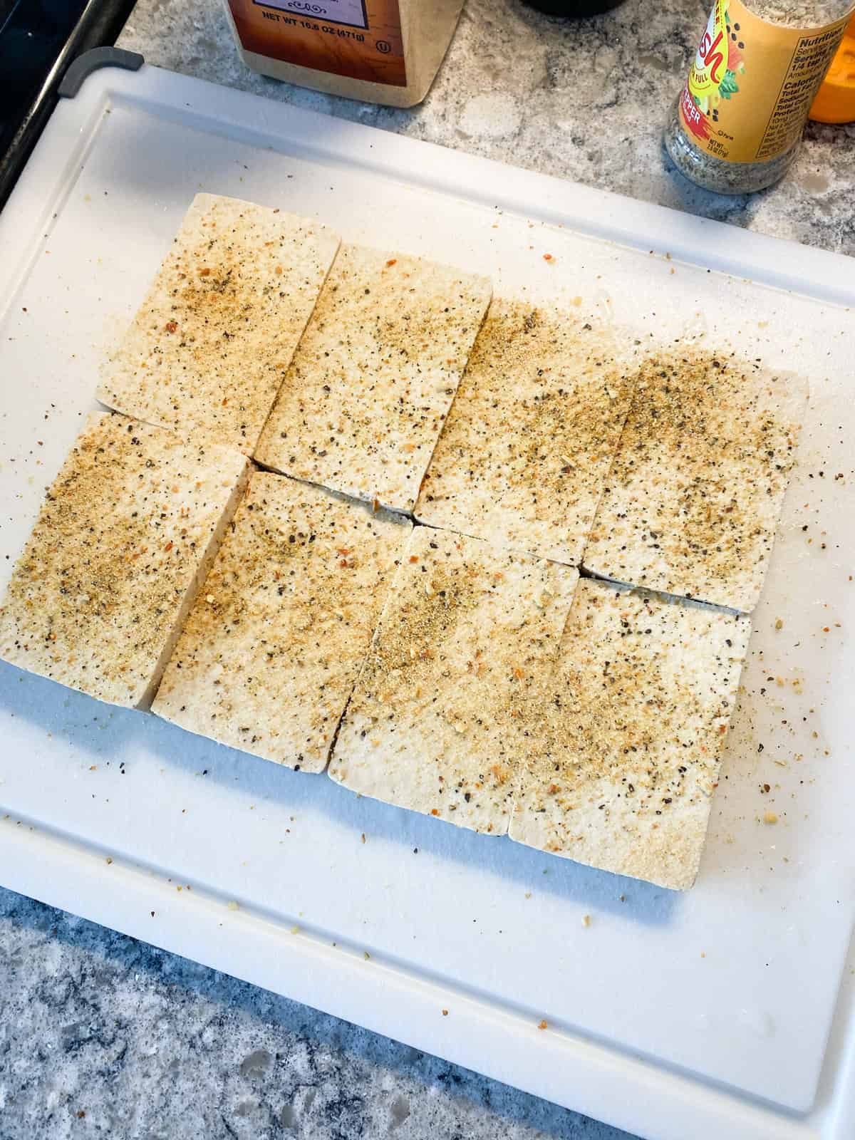 Slices of tofu on a cutting board, sprinkled with seasoning.