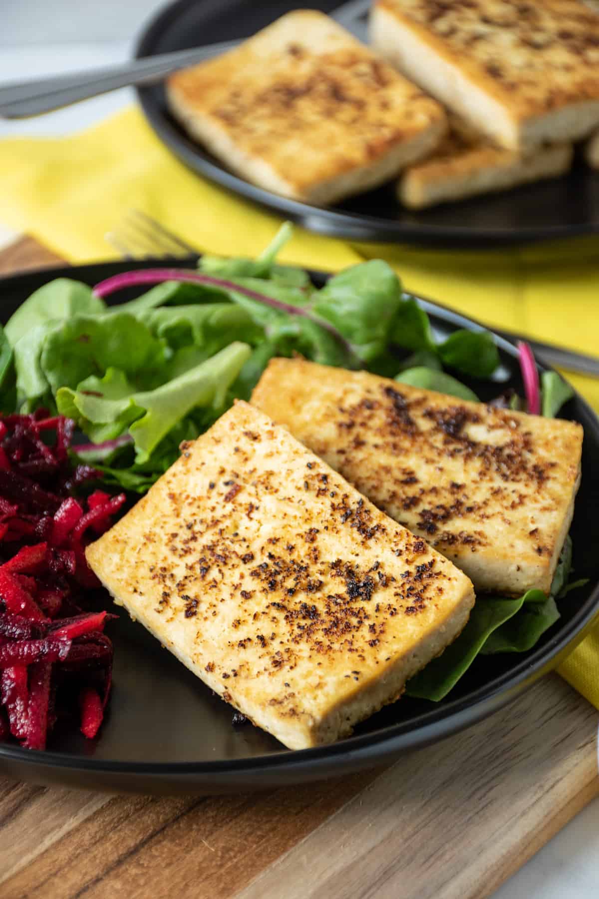 2 slices of cooked tofu over a bed of greens, with a side of shredded beet salad.