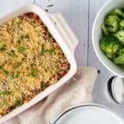 Overhead image of a casserole in a casserole dish, with a bowl of steamed broccoli nearby.