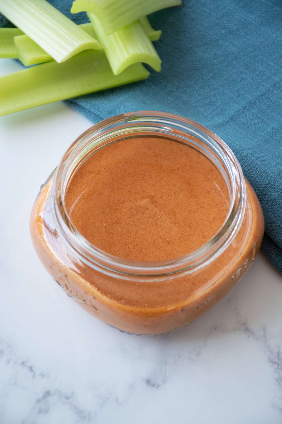 Buffalo sauce in a small jar, with celery sticks in the background.